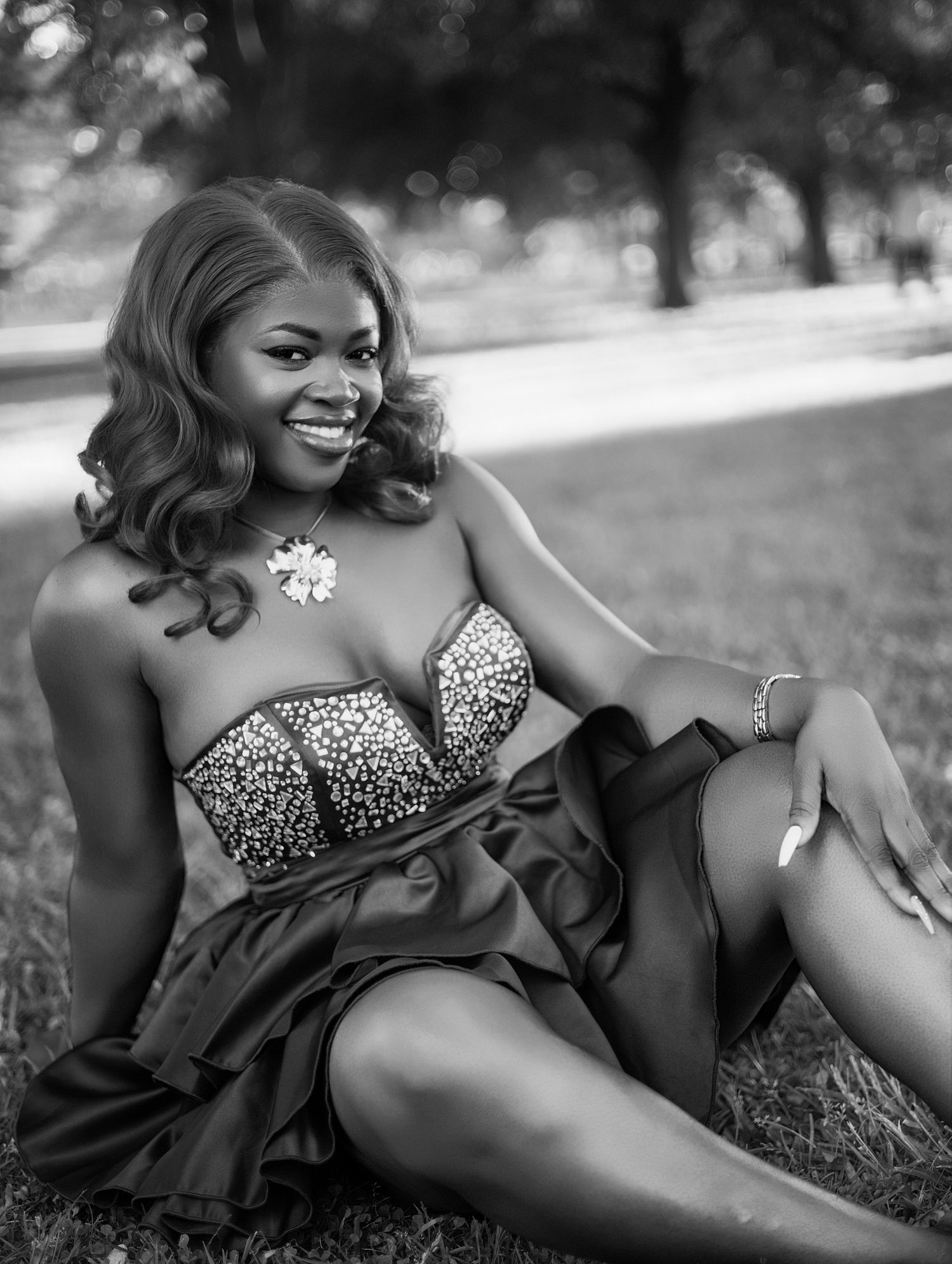 Black and white photo of joyful woman in sparkly strapless dress relaxing on grass in park in unique birthday photoshoot toronto