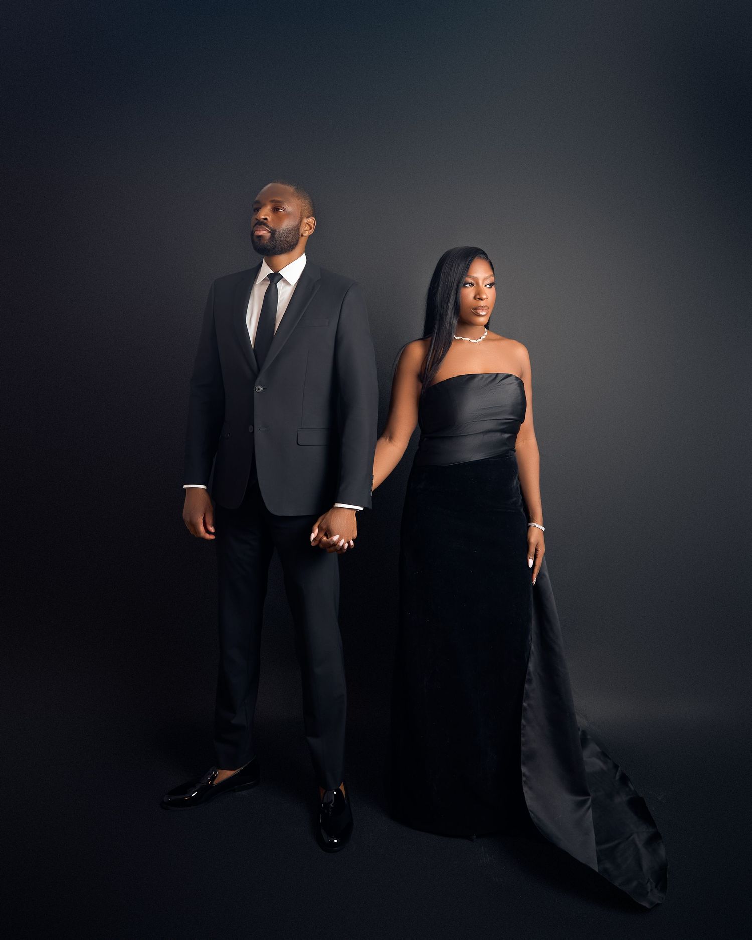 Stylish couple holding hands in formal wear, posing dramatically against a dark studio backdrop in intimate birthday photo session toronto