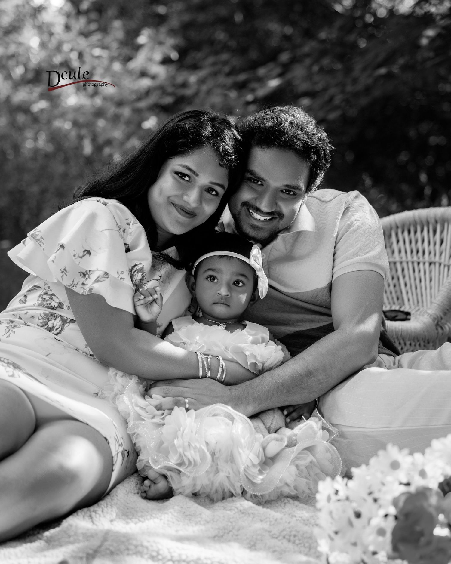 Black and white portrait of smiling South Asian couple lying with baby in white ruffled outfit captured by Downtown Toronto family photograp