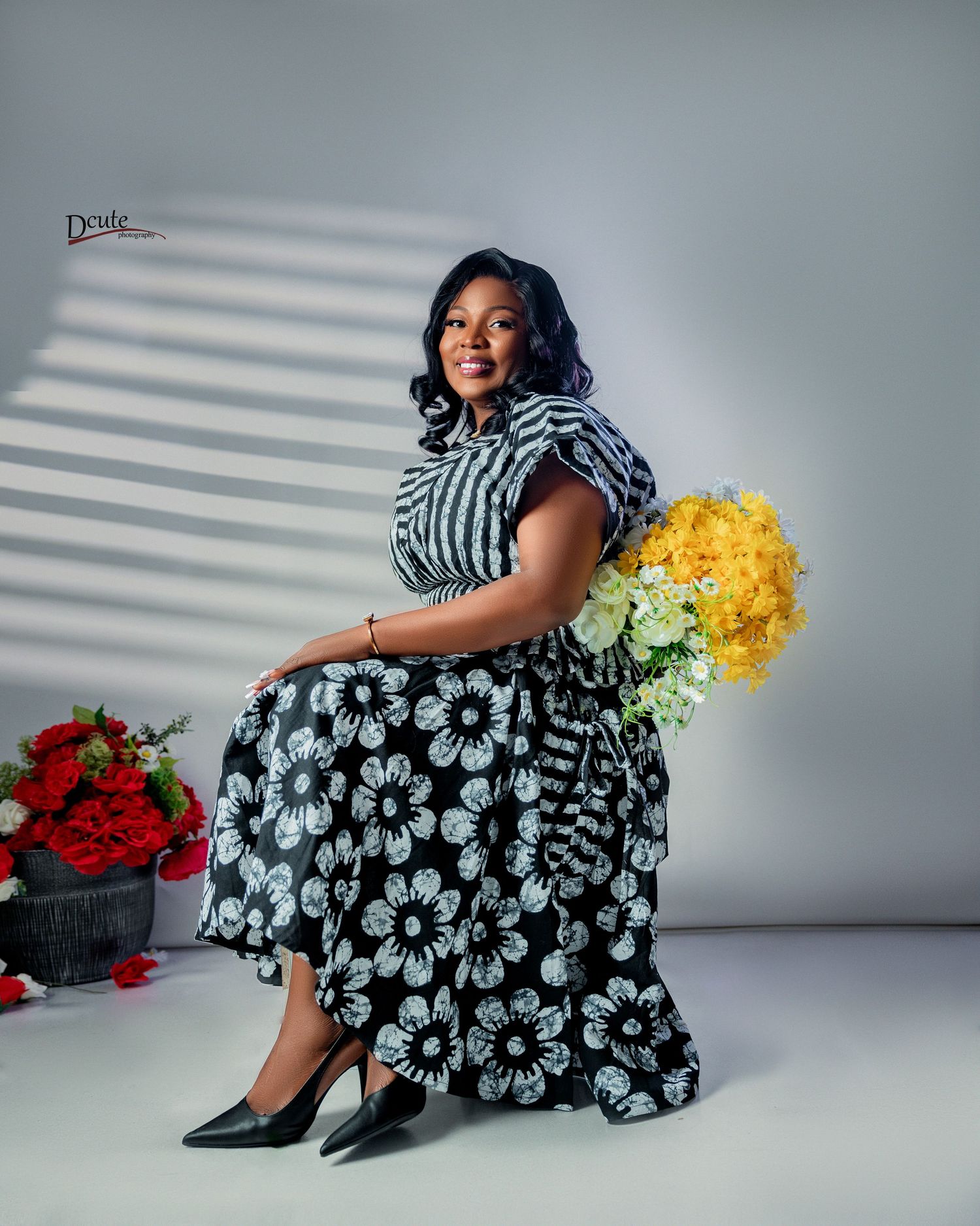 An elegant woman in a black and white floral dress sits gracefully holding yellow and white flowers in a family photoshoot idea in toronto
