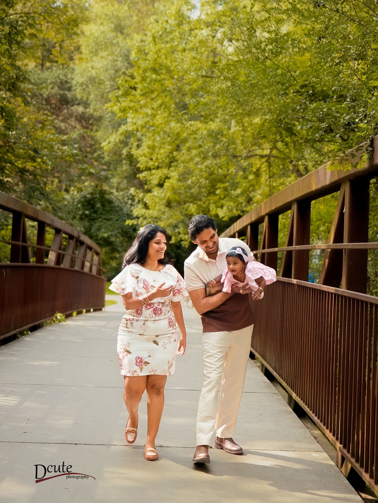 Happy family walking on a bridge surrounded by lush green trees during a professional outdoor family photo session in downtown toronto