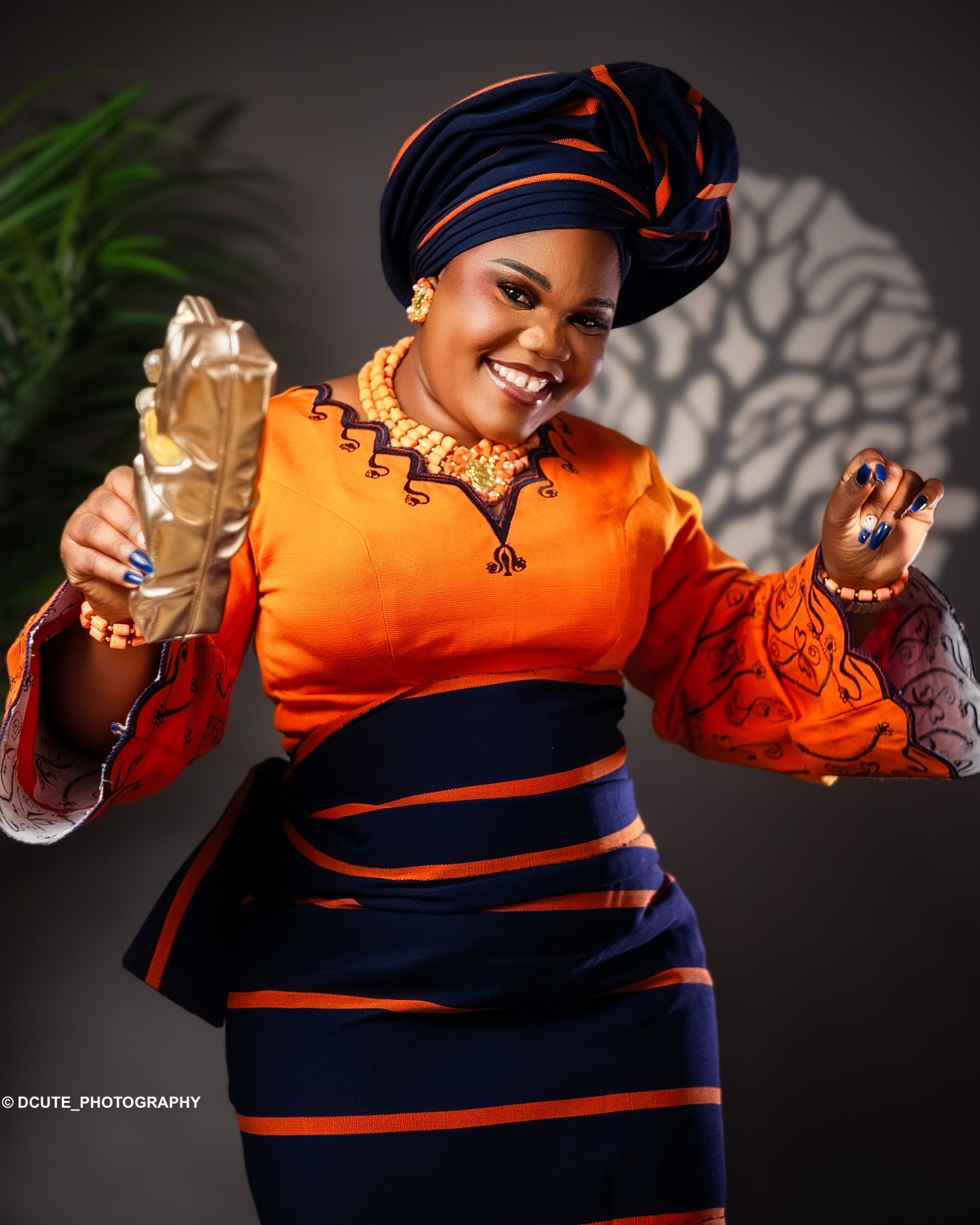 Woman in vibrant orange and navy African attire holding an award trophy in birthday photography packages toronto
