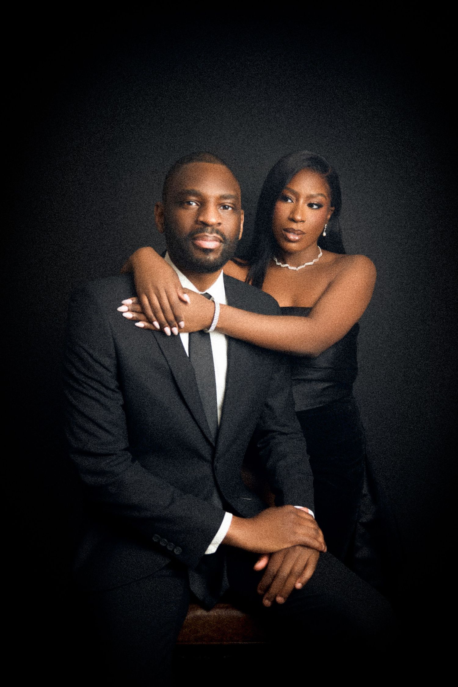 Couple in black formal wear posing intimately in a dark studio, woman resting arms on shoulders in intimate birthday photo session toronto