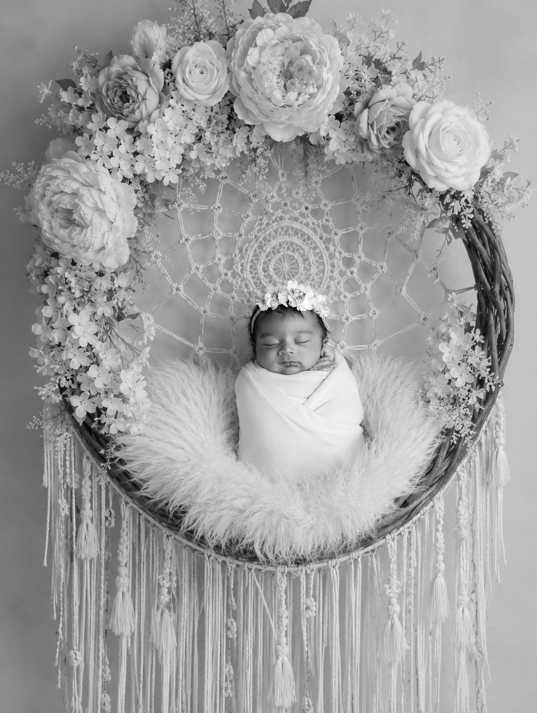 Black and white newborn photo of swaddled baby in floral wreath dreamcatcher prop Newborn photography in Toronto