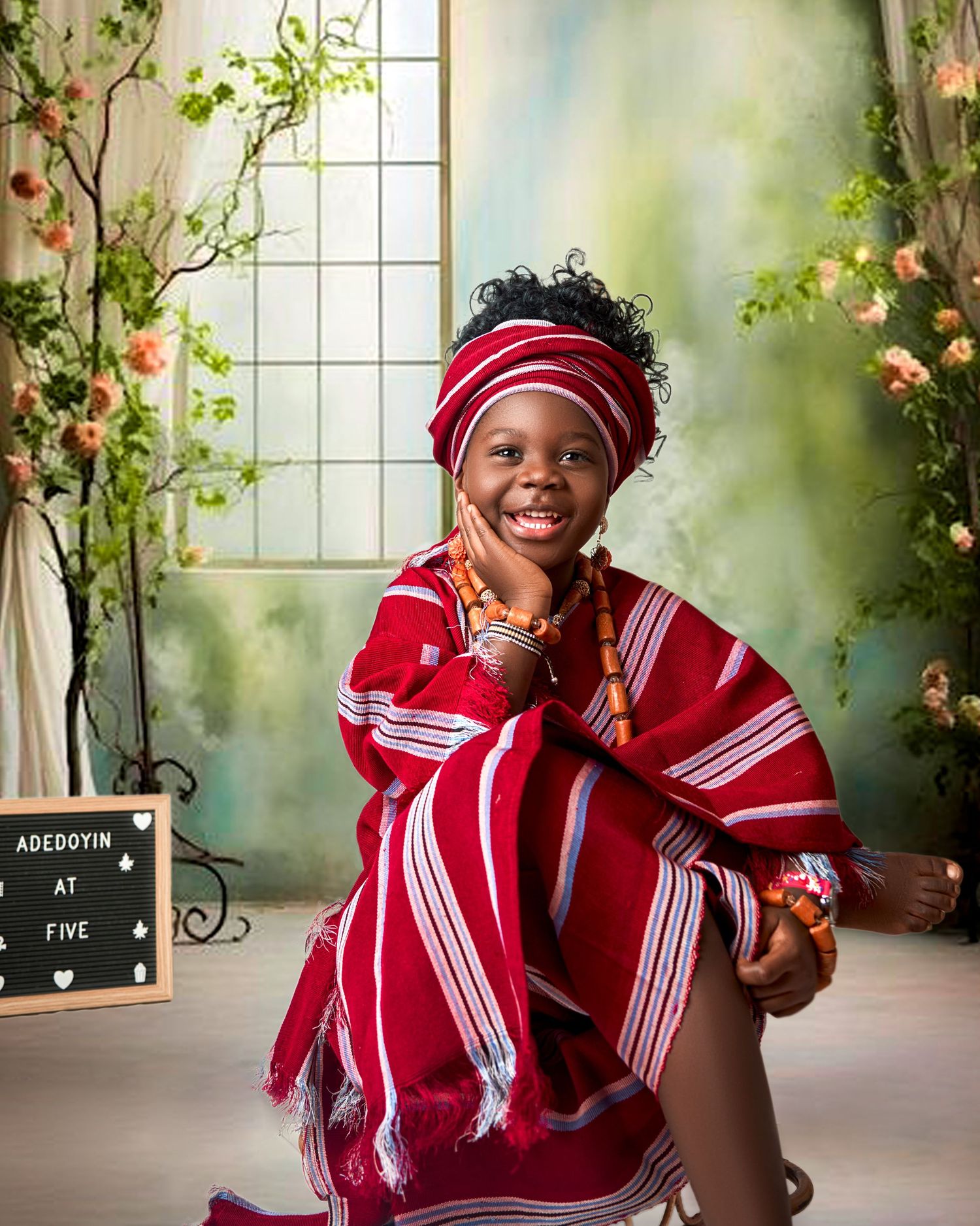 Joyful young girl in red and white traditional African outfit celebrates her fifth birthday milestone.