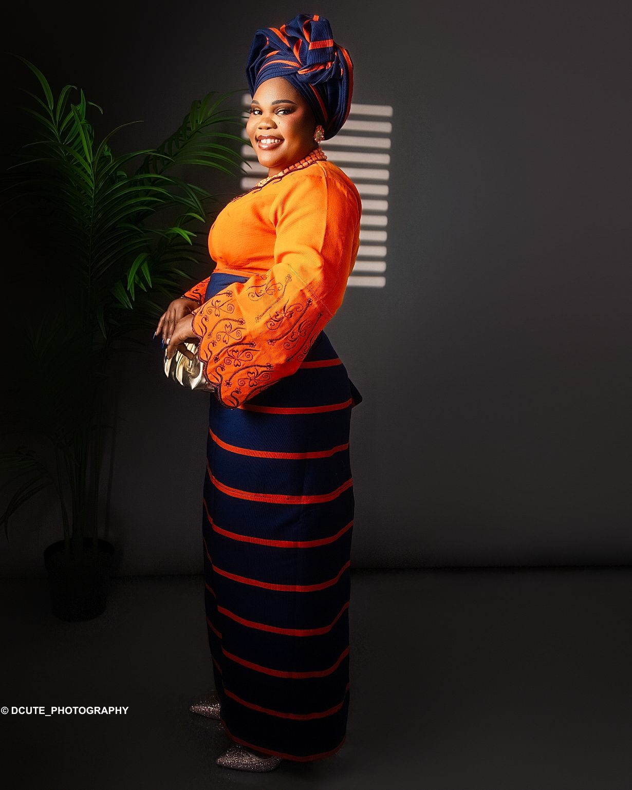 Woman in orange and navy African print outfit with matching gele poses in studio portrait in toronto