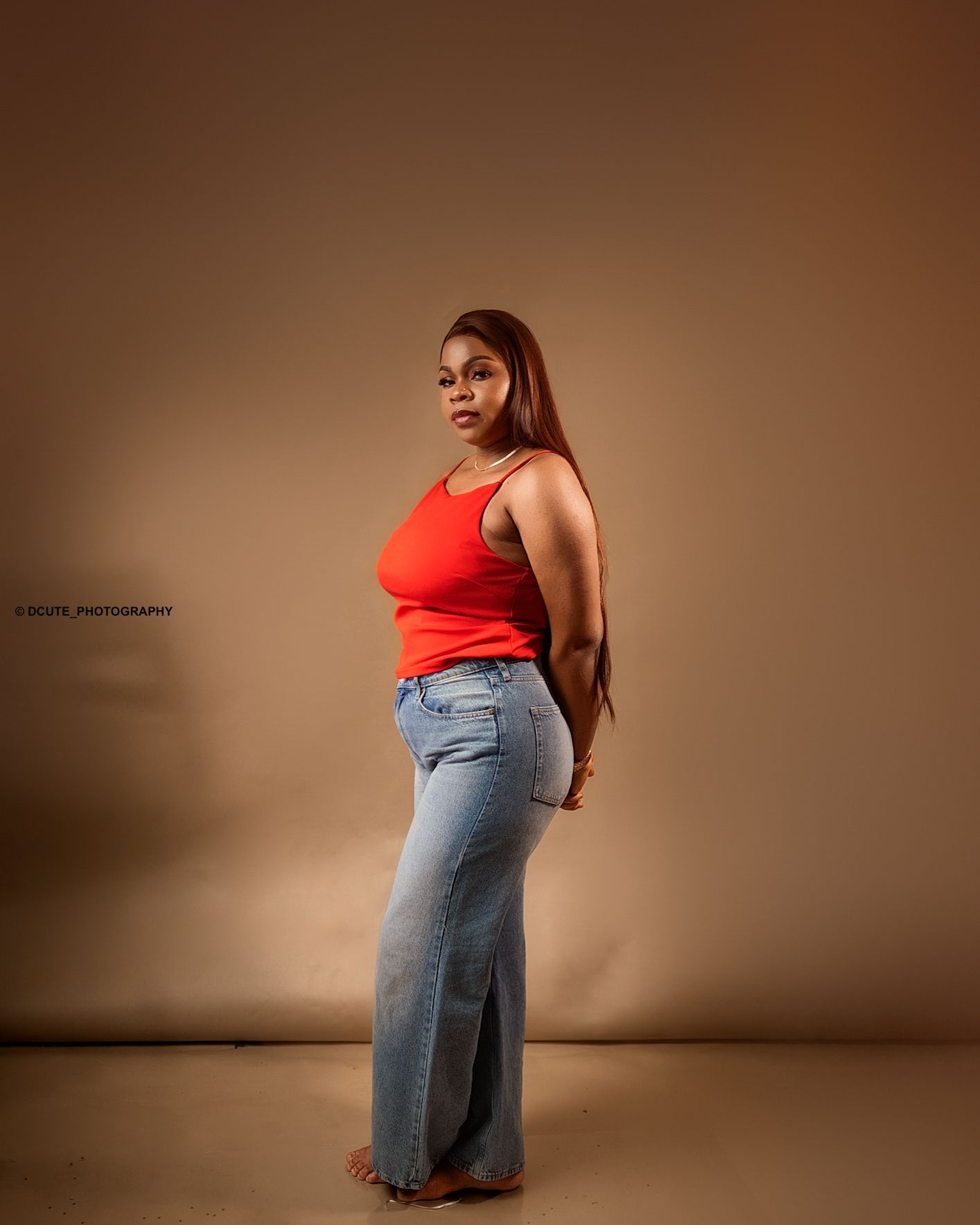 Woman in red tank top and wide-leg jeans posing in profile against a warm beige studio background by best birthday photographer toronto