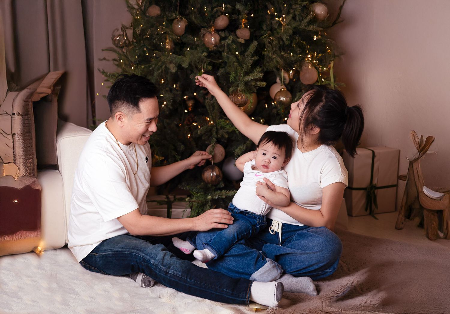 parents and baby enjoy a festive moment decorating a glowing Christmas tree together in a holiday family photography near Downtown Toronto