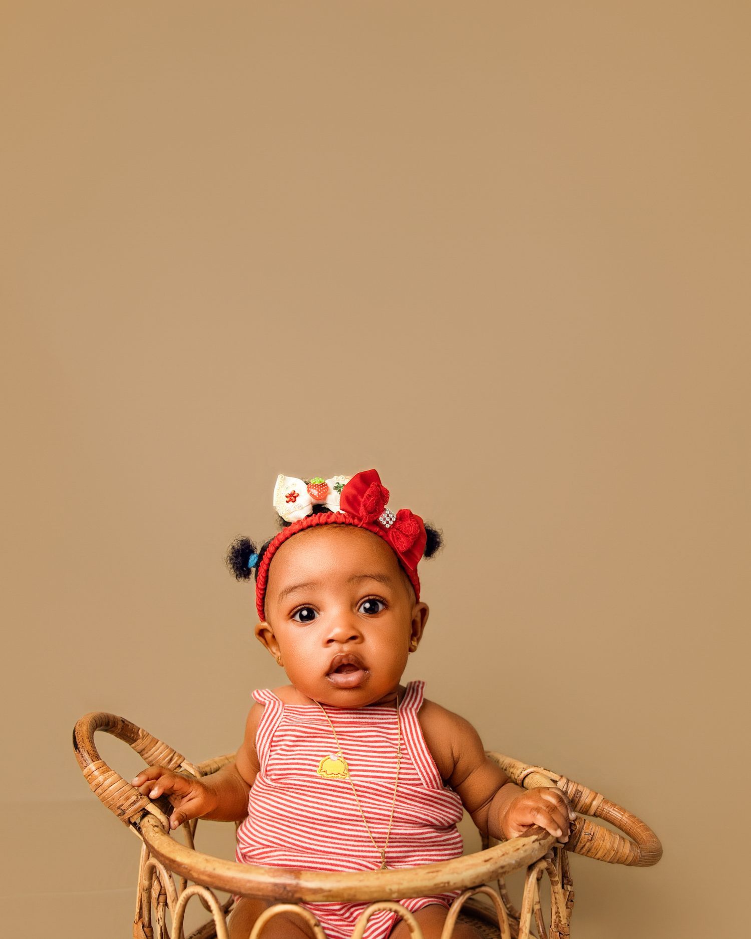 A baby girl wearing a floral headband sits in a rattan basket wearing a pink striped outfit.