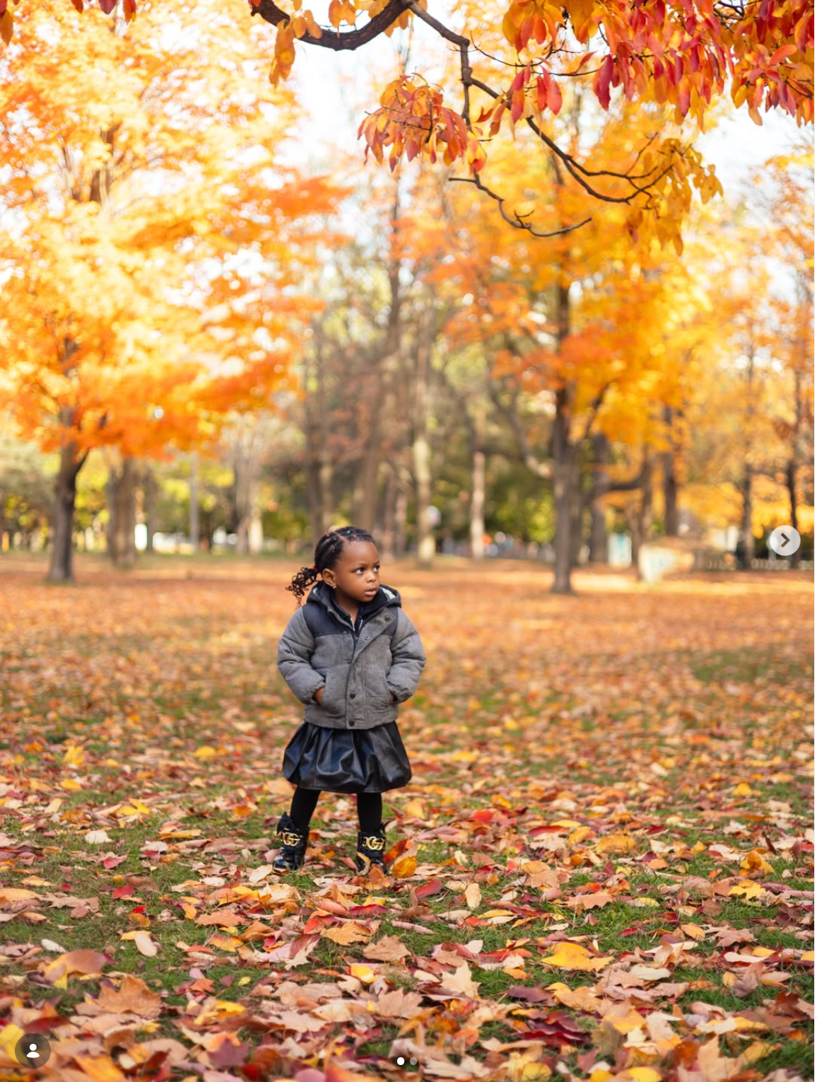 Young girl in gray jacket and black skirt standing among vibrant orange autumn leaves in a park best birthday photographer toronto
