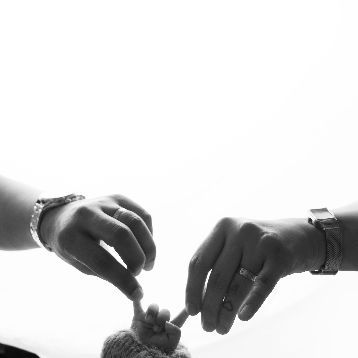Black and white photo of parents hands gently holding their newborns tiny fist together.