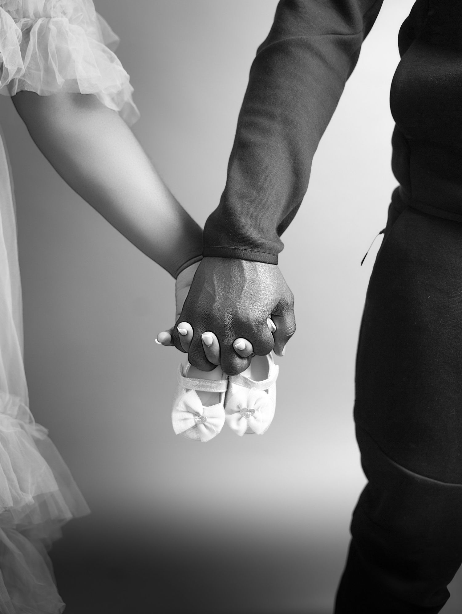 Black and white photo of couple holding hands with white baby booties between them captured by a maternity photographer in toronto