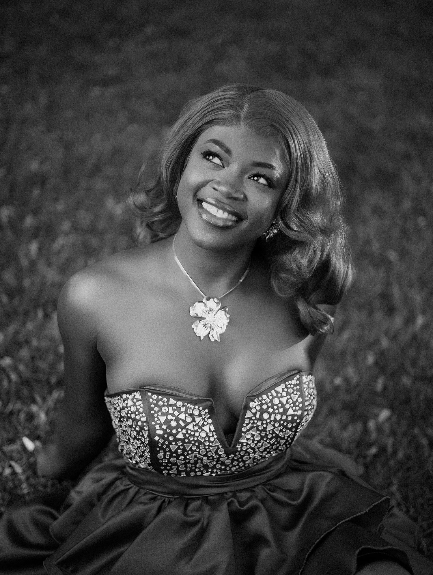 Black and white portrait of smiling woman in bedazzled strapless gown seated on grass in outdoor birthday photoshoot in toronto