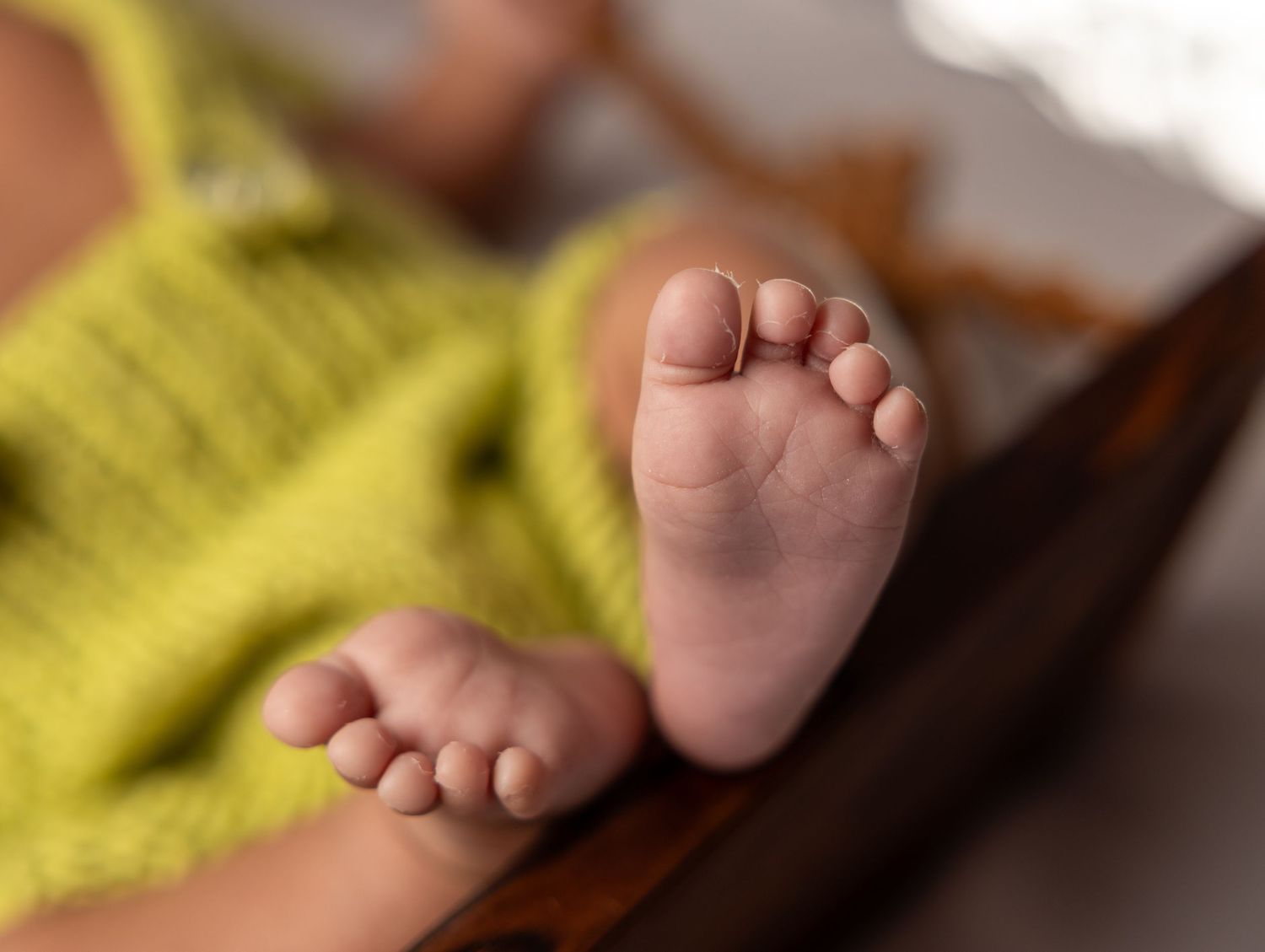 Close-up of newborn baby feet in yellow knit wrap on wooden surface.