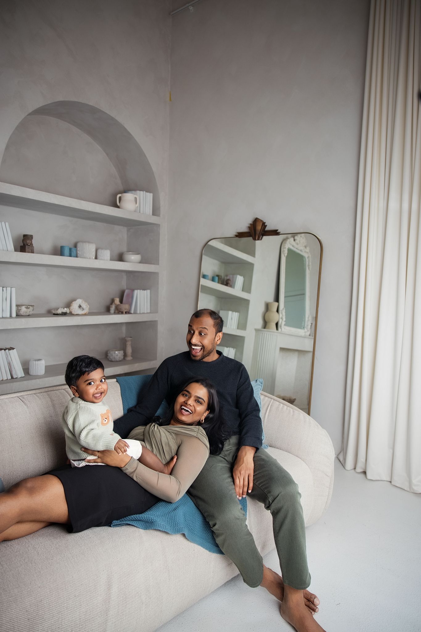 A happy family of three relaxes on a cozy white sofa in a modern gray living room in Family photos in Downtown Toronto