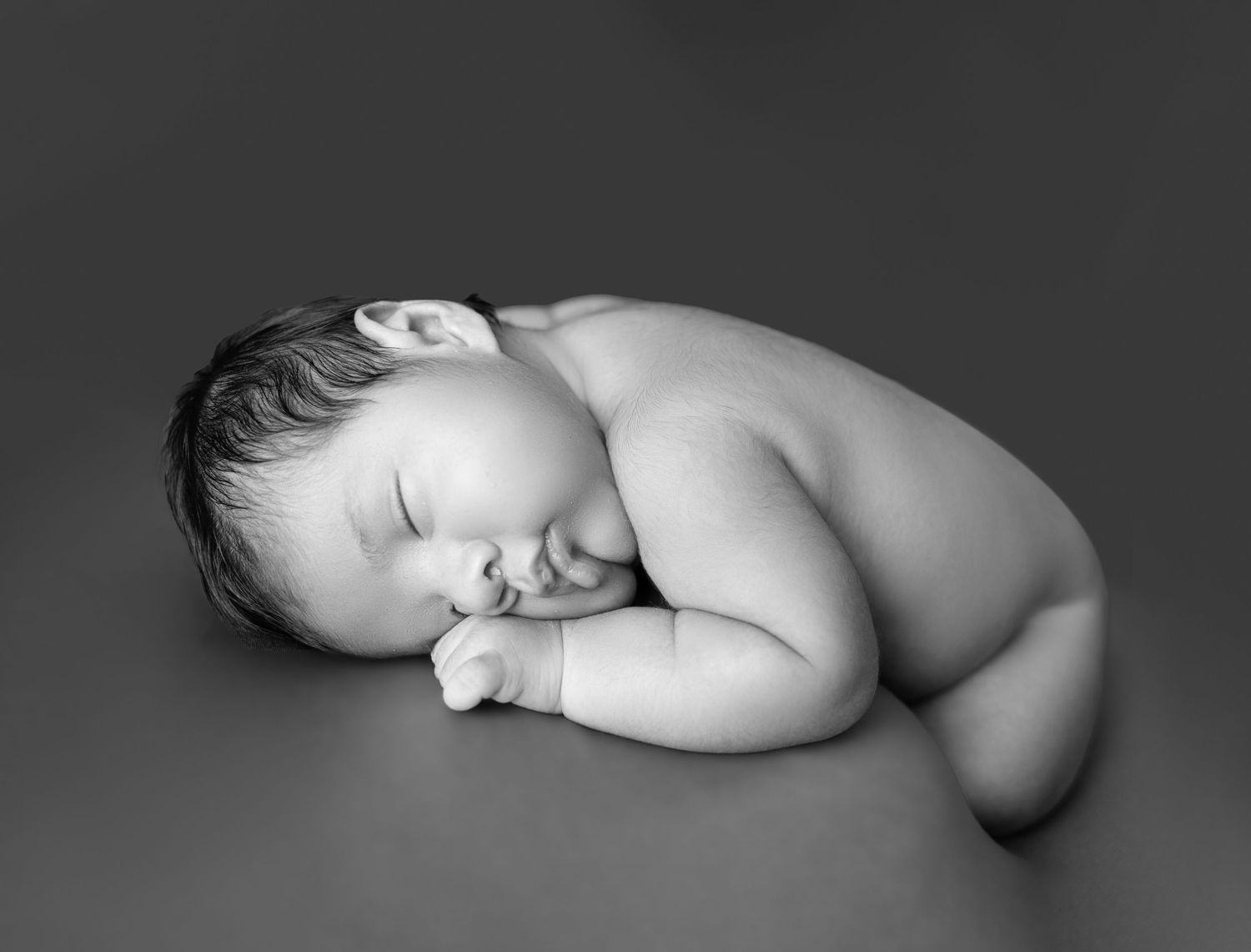 Black and white sleeping newborn baby photoshoot in toronto, he is curled in fetal position on surface.
