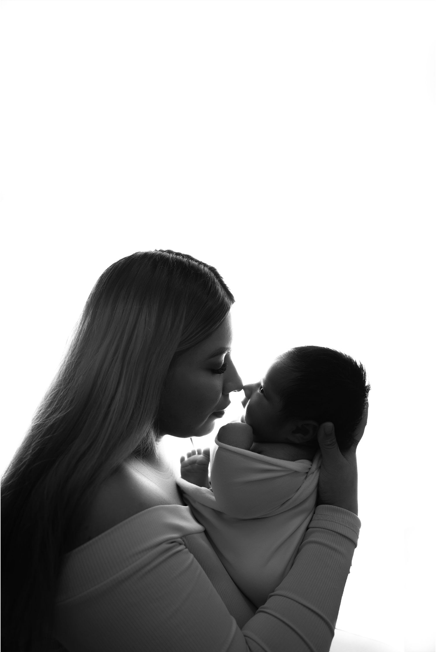 Black and white photo of a mother tenderly holding her newborn baby close, touching noses in an intimate moment.