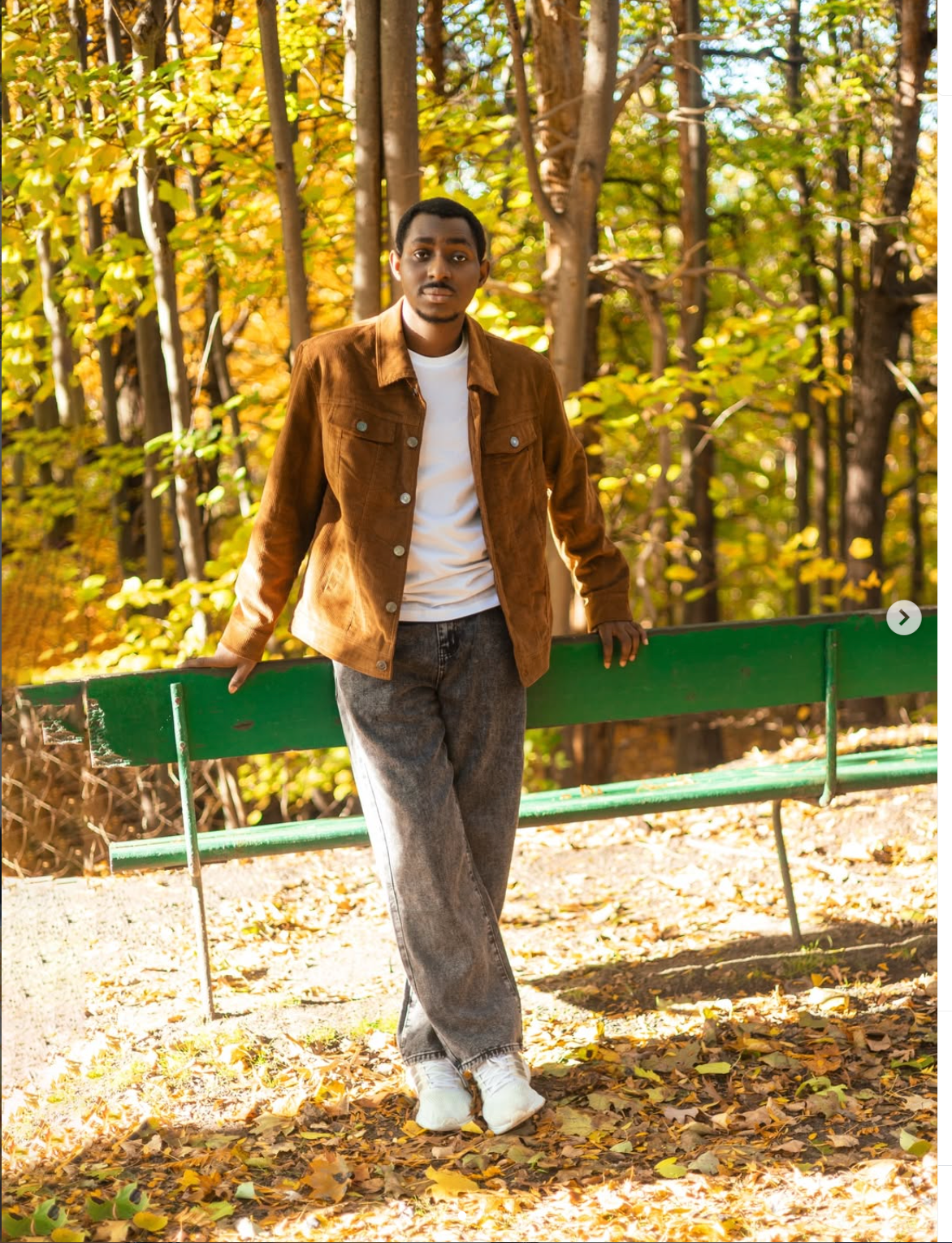 Young man in brown suede jacket and gray pants walking along a leaf-covered autumn park path by the best birthday photographer toronto