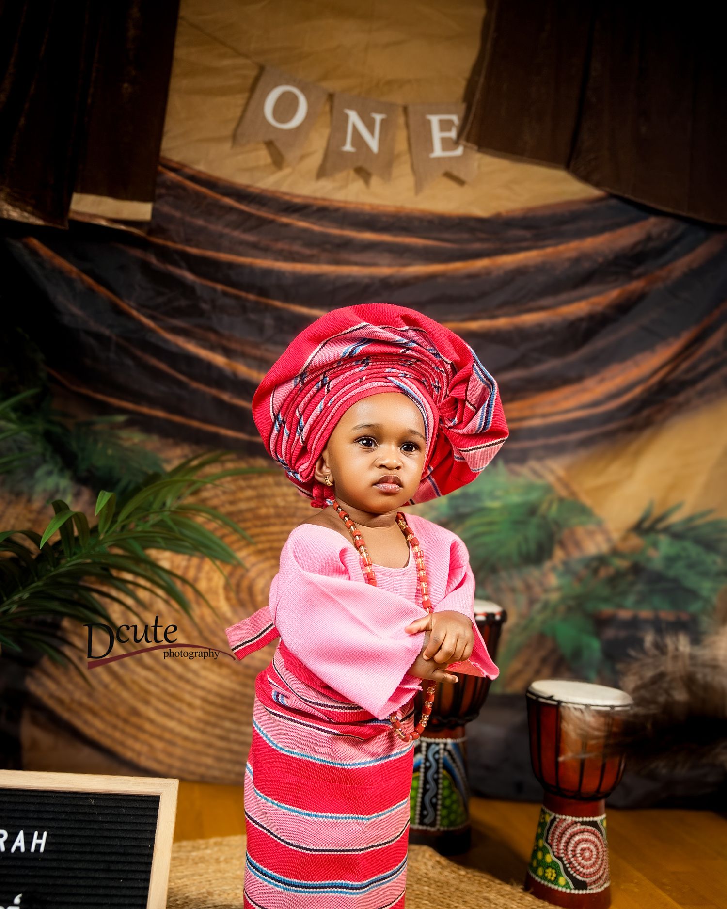 Toddler girl in vibrant pink African traditional attire celebrating her first birthday with djembe drums.