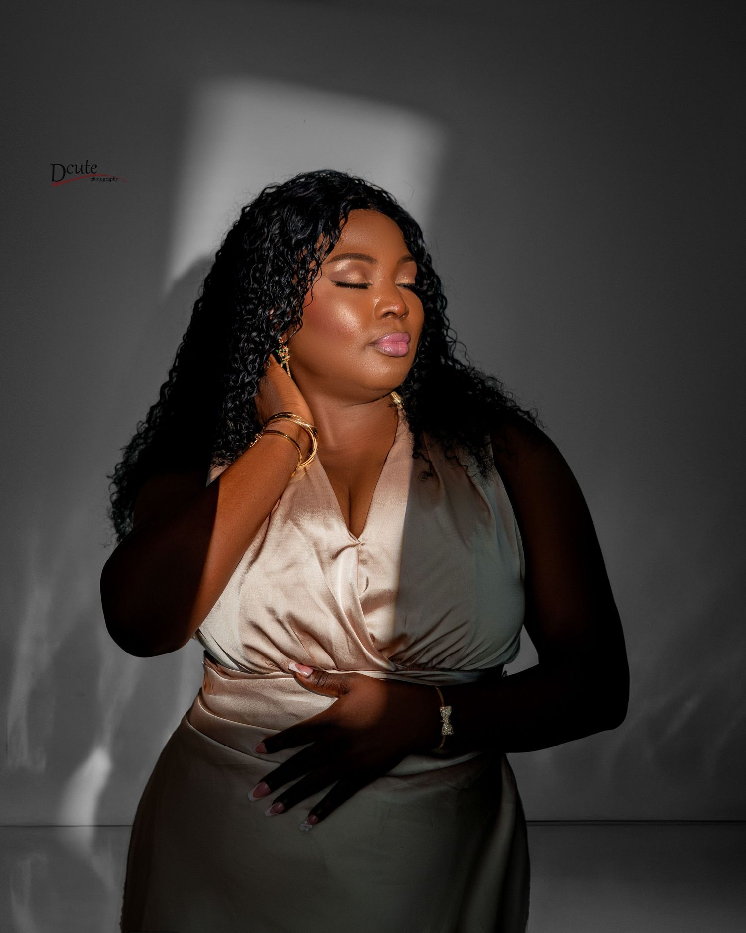 Woman in champagne satin top and black gloves poses in dramatic studio lighting portrait.
