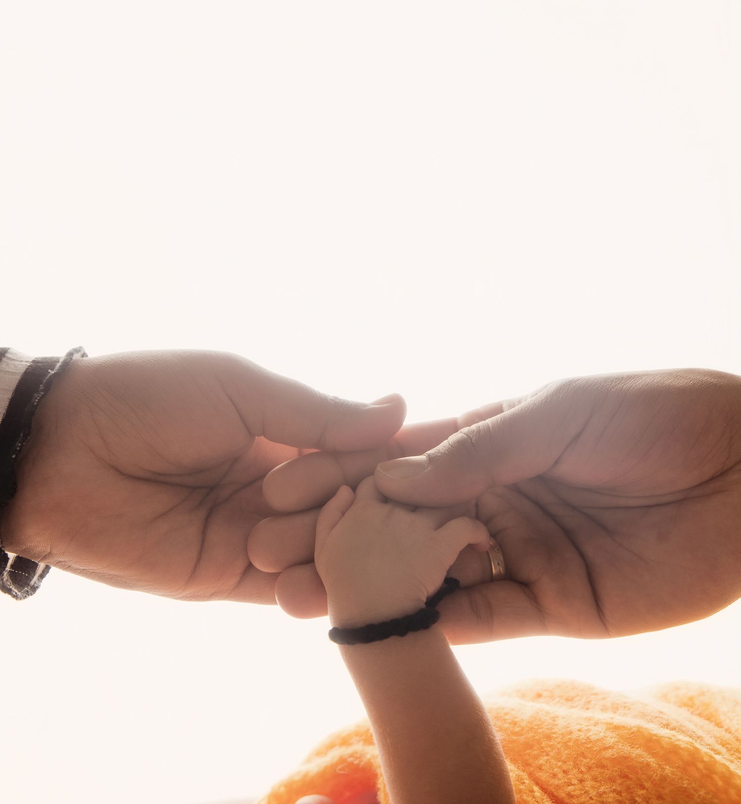 Two adults gently holding a small childs hand together in a tender moment of connection.