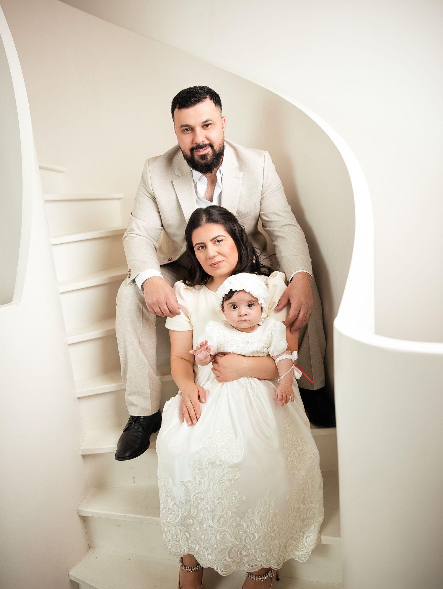 Family portrait of parents and baby in white lace dress seated on curved white stairs Family portrait photographer Downtown Toronto