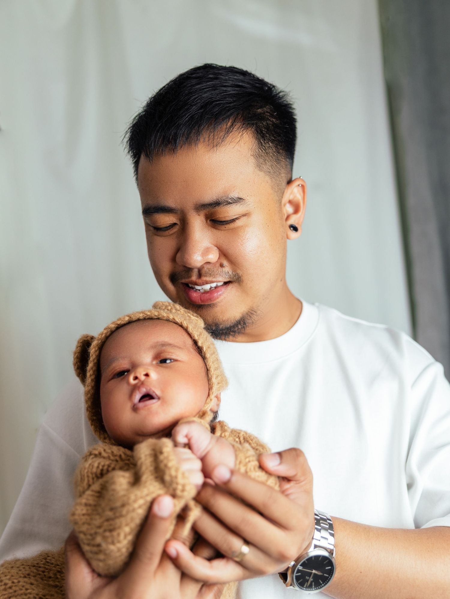 Young father in white t-shirt holding his newborn baby dressed in brown bear knit costume in a Newborn photographer in Toronto home session