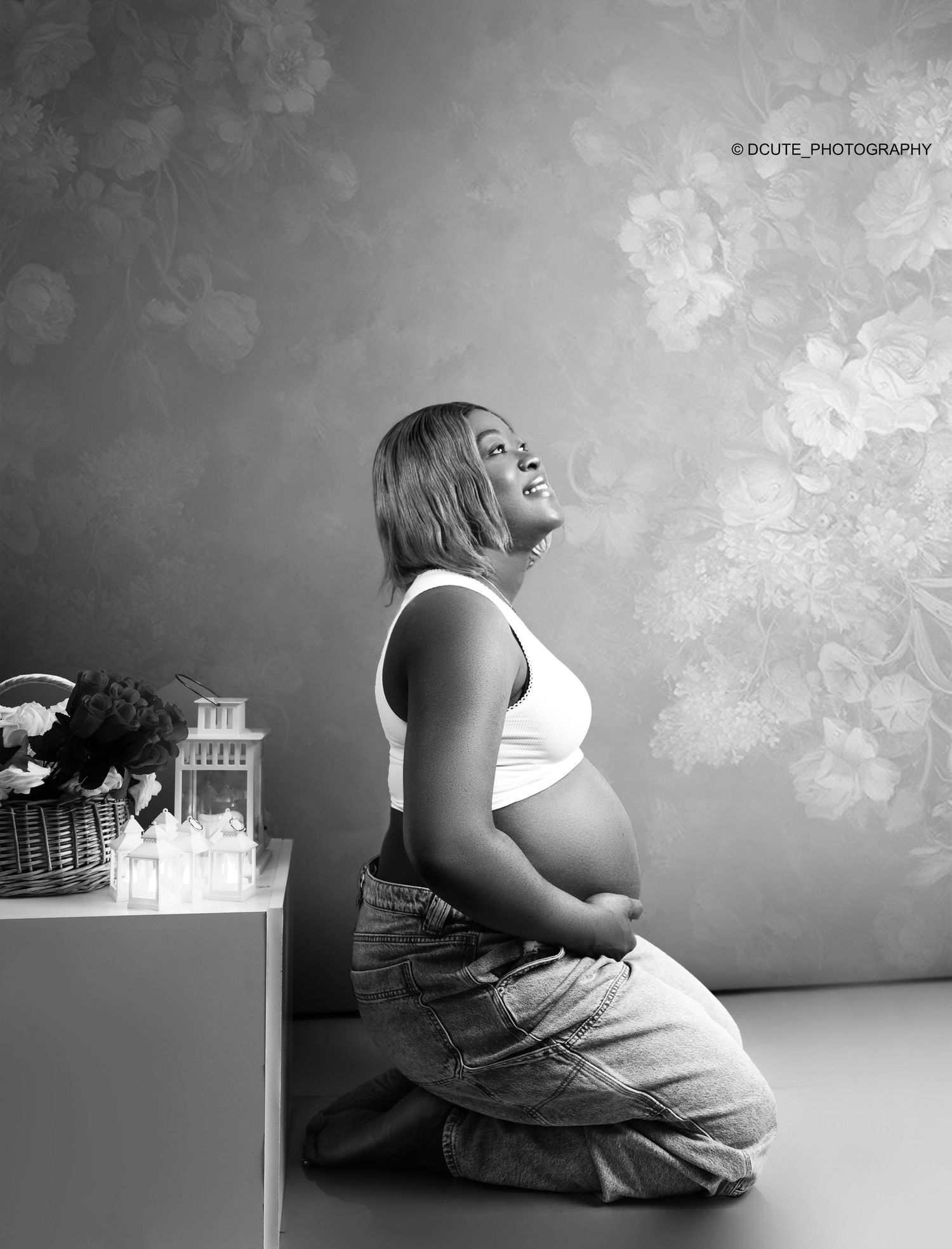 Black and white maternity portrait of smiling pregnant woman kneeling in jeans in studio maternity photography toronto