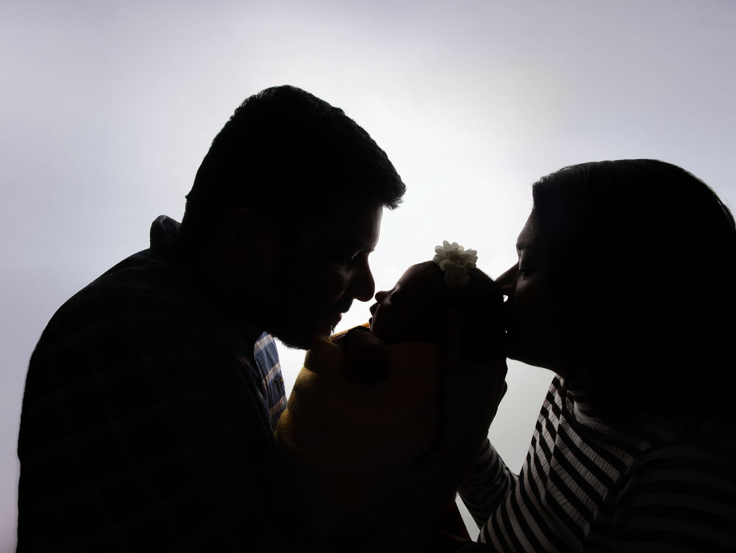 Silhouette of couple sharing a kiss with a flower against bright backlit sky.
