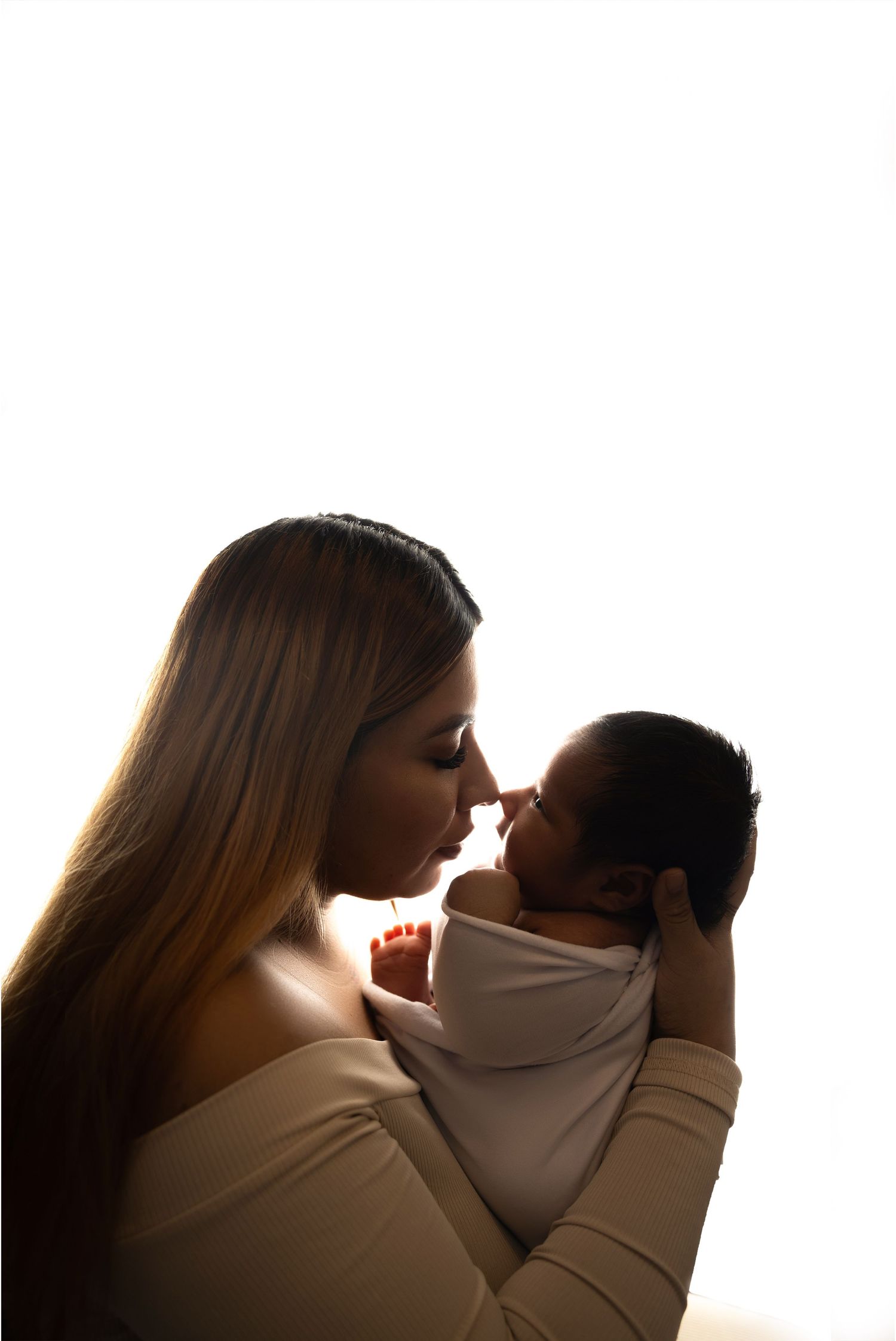 Silhouette of mother holding newborn baby photography in toronto close to her face near bright window.