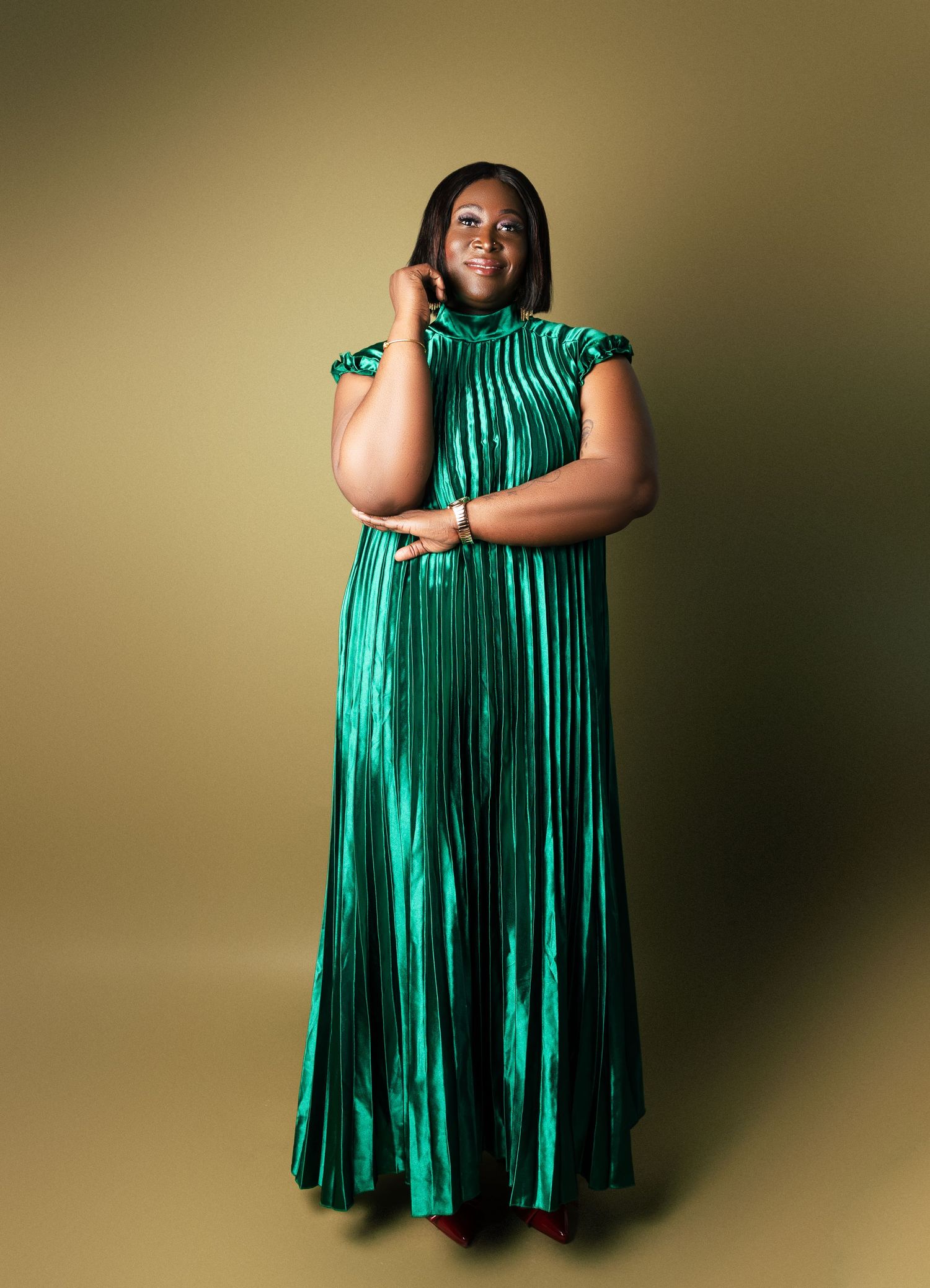 Woman in elegant emerald green pleated metallic maxi dress posing against golden background n relaxed outdoor birthday photos toronto