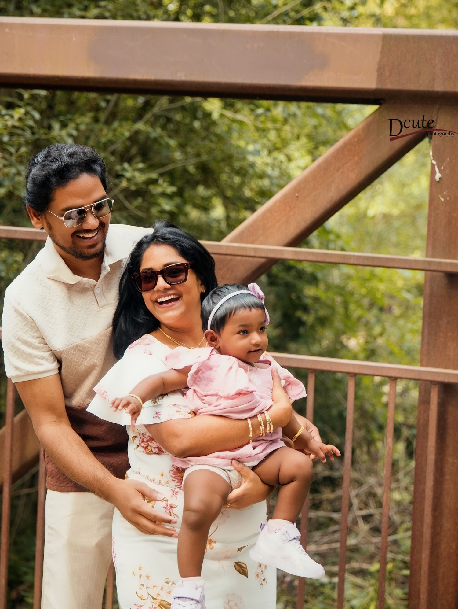 Happy South Asian family with mother holding baby girl in pink dress on wooden bridge outdoors by a Family photographer in Downtown Toronto