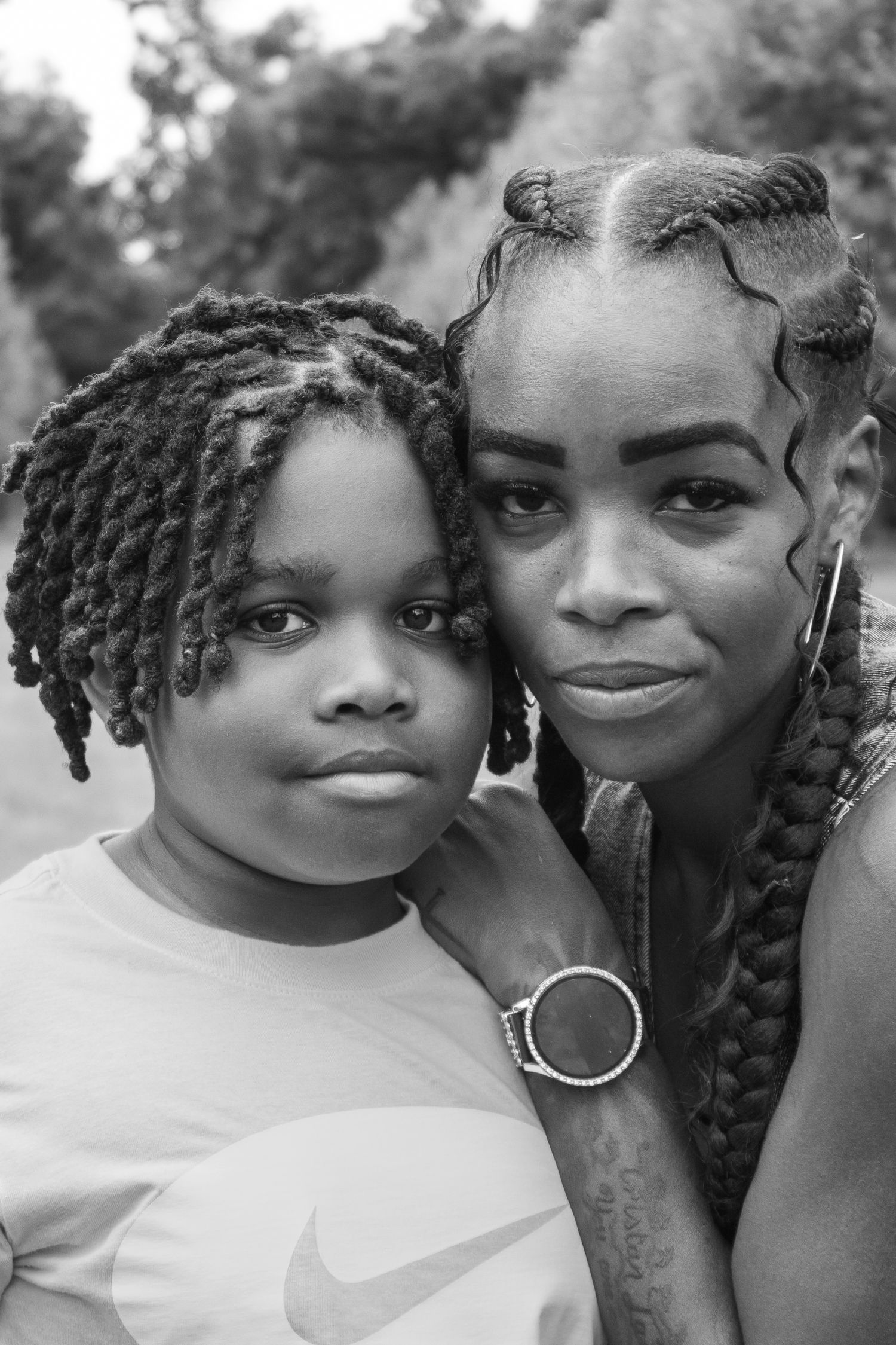 A black and white portrait of a mother and child posing cheek to cheek outdoors.