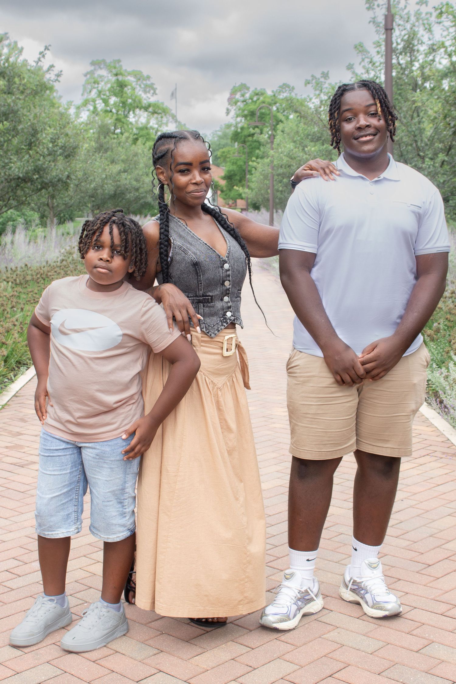 Mother in a tan dress smiling with her two children on a park pathway during a natural outdoor family photography session.