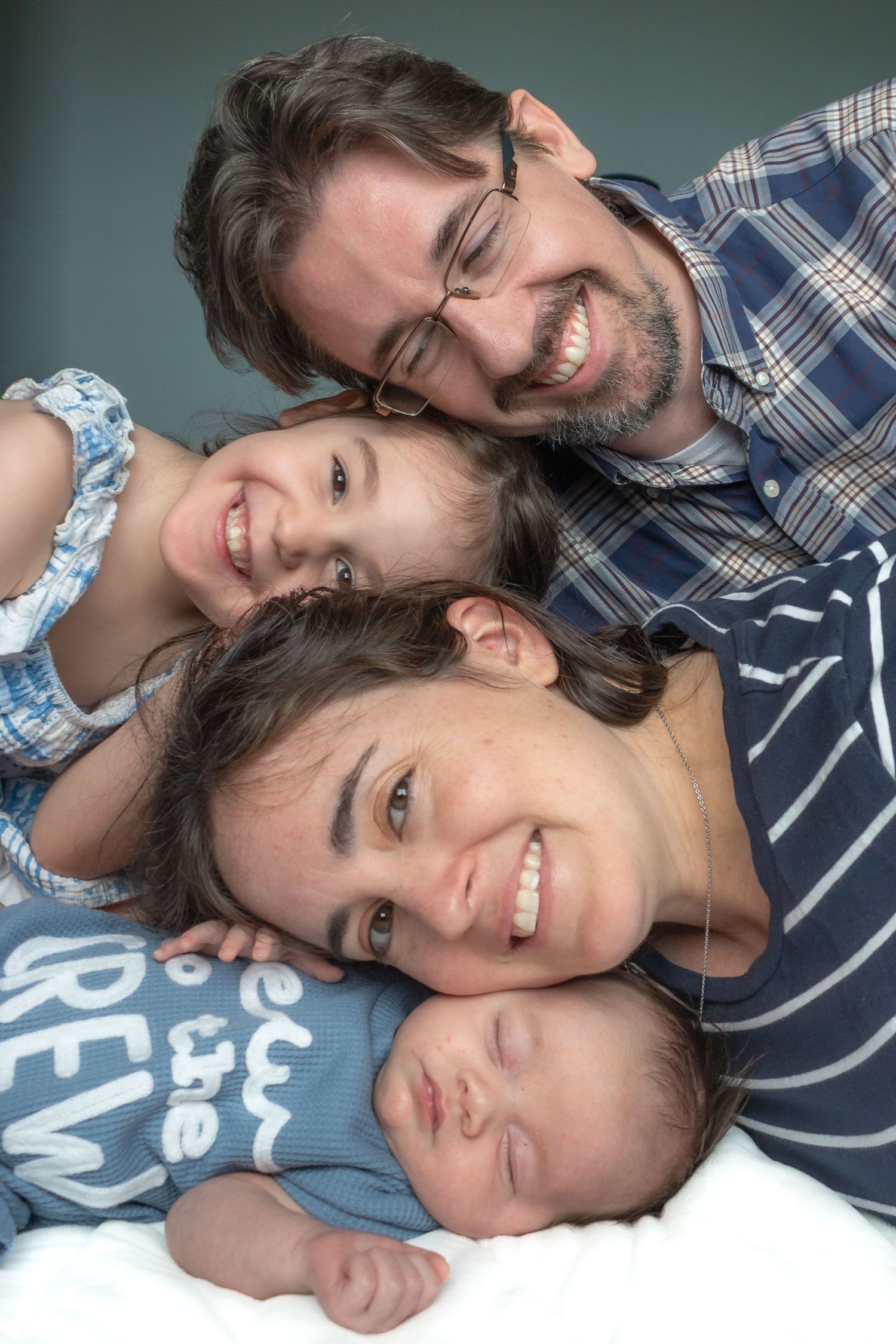 Smiling parents and young daughter cuddling their newborn baby during a cozy lifestyle family photography session at home.