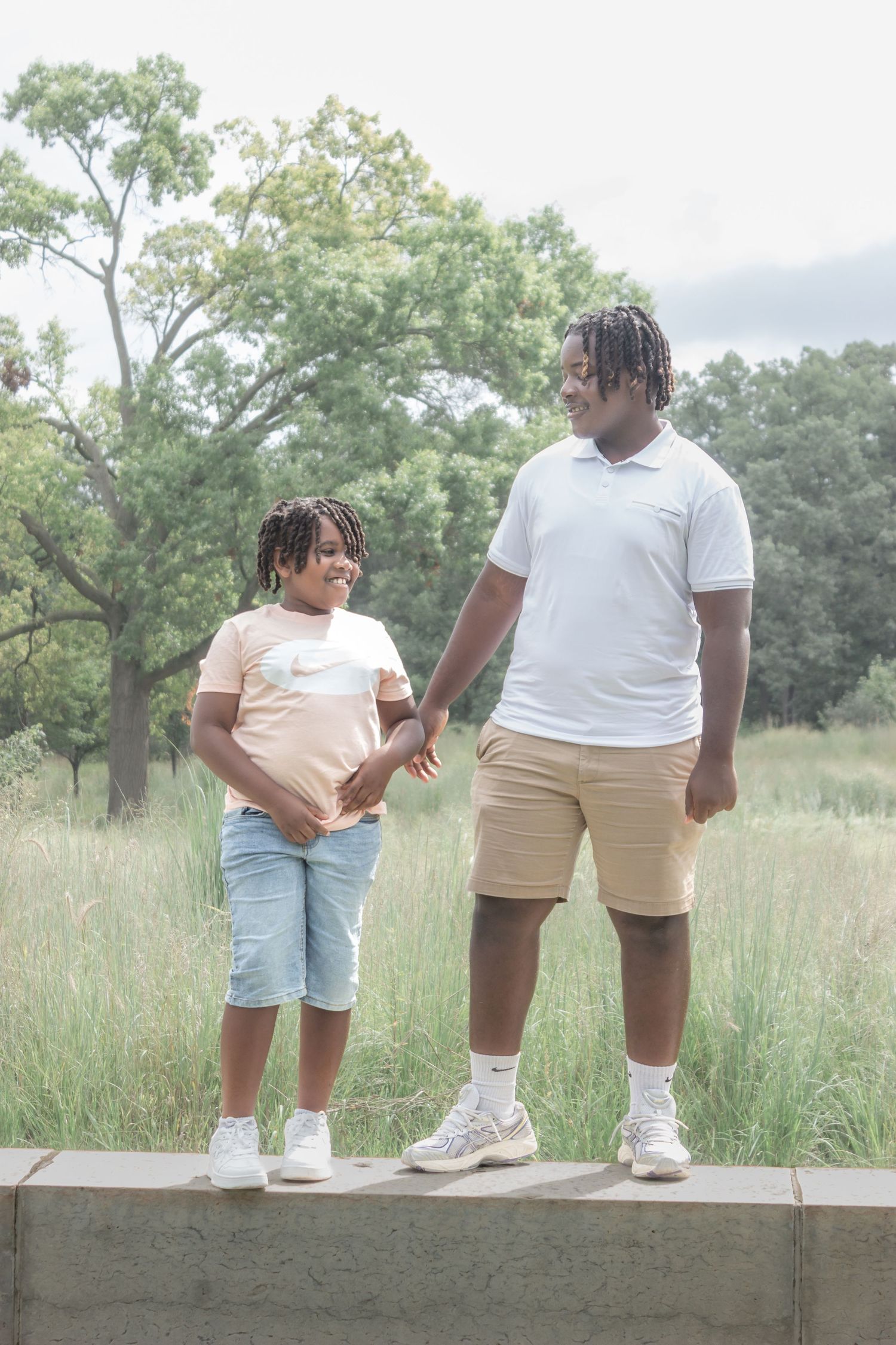Mother and son holding hands on a stone wall in a grassy park during a natural outdoor family portrait session.