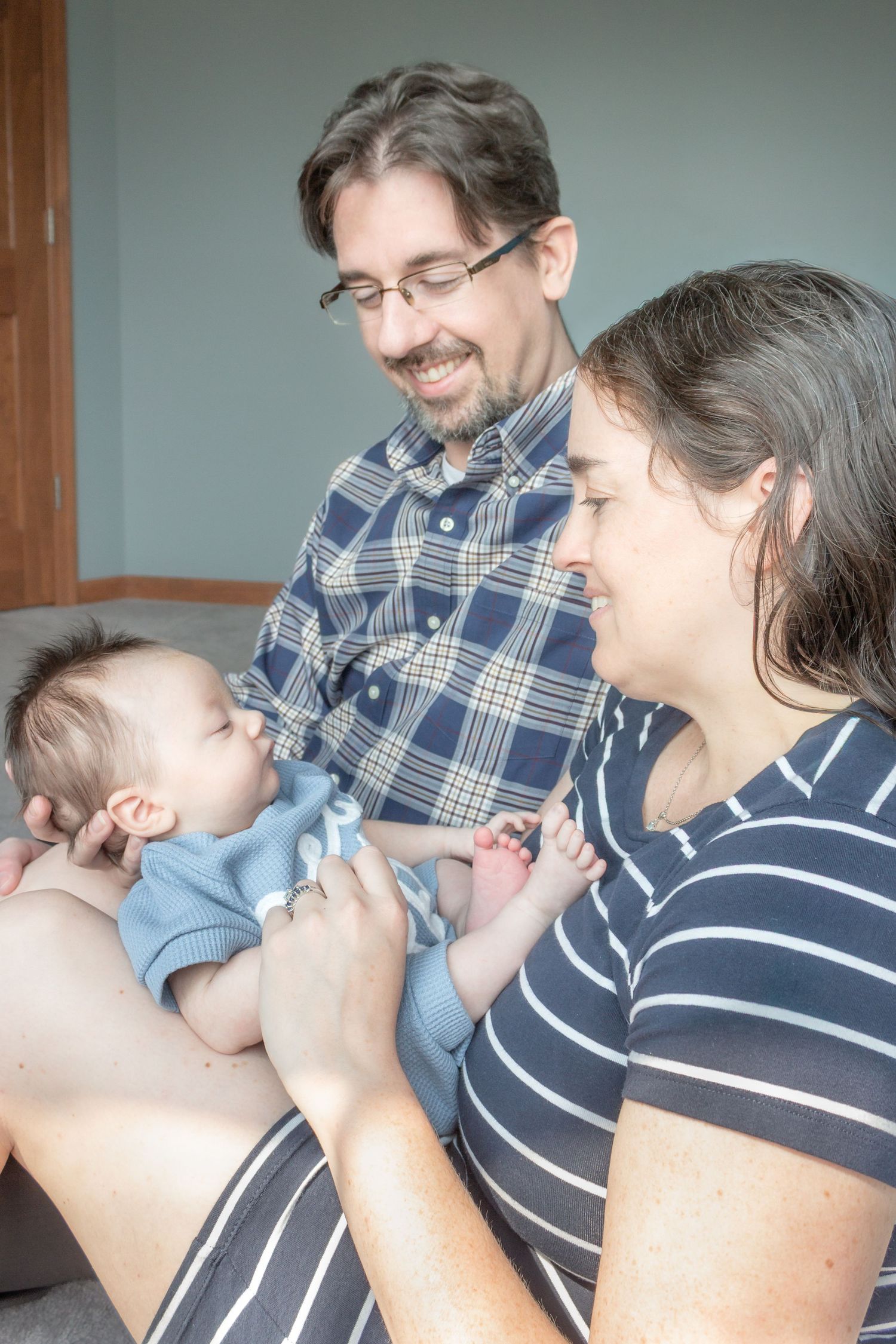 Smiling parents gazing lovingly at their baby during a relaxed in-home newborn family photography session.