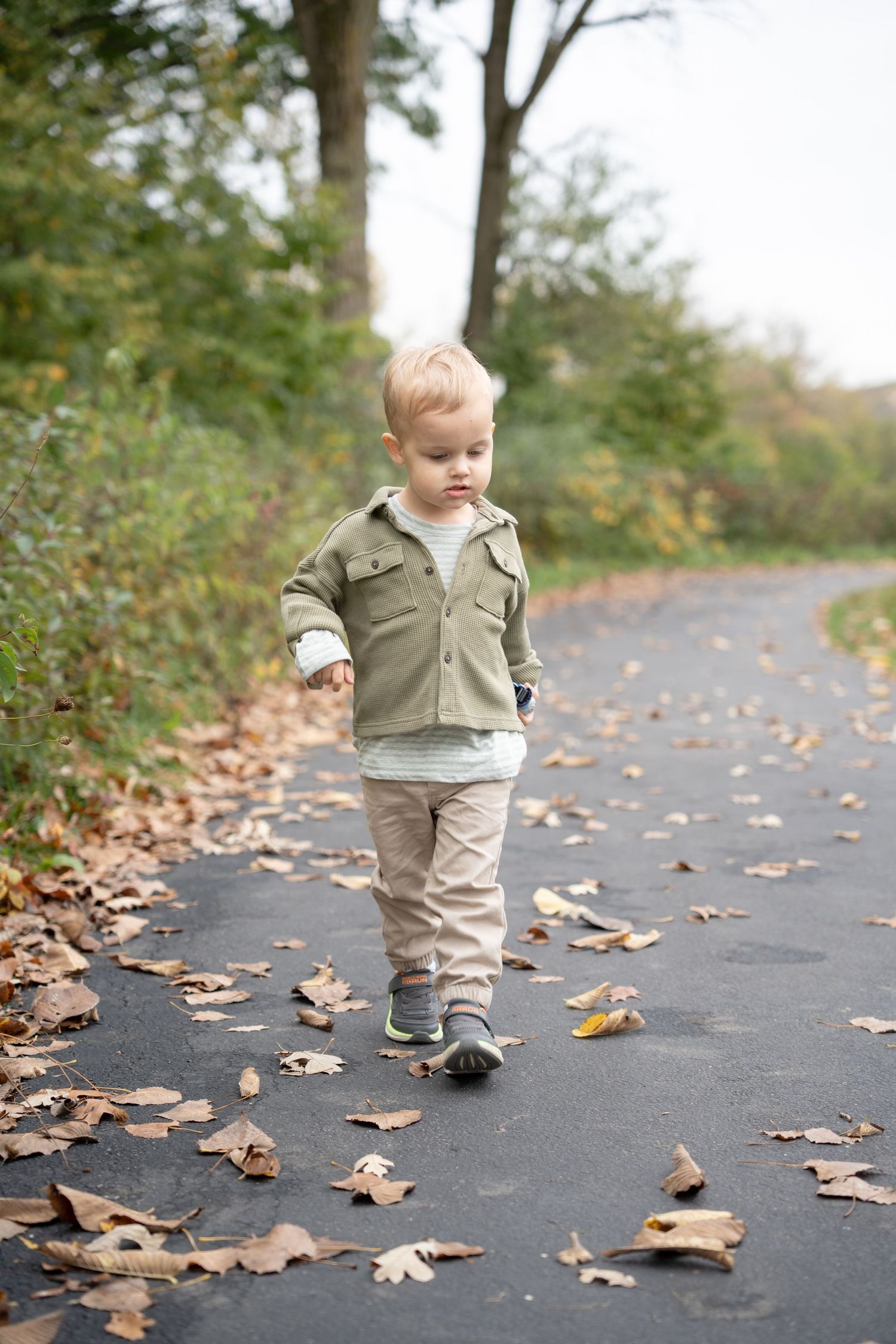 Young boy walking along a paved path covered in fallen autumn leaves during an outdoor fall photography session.