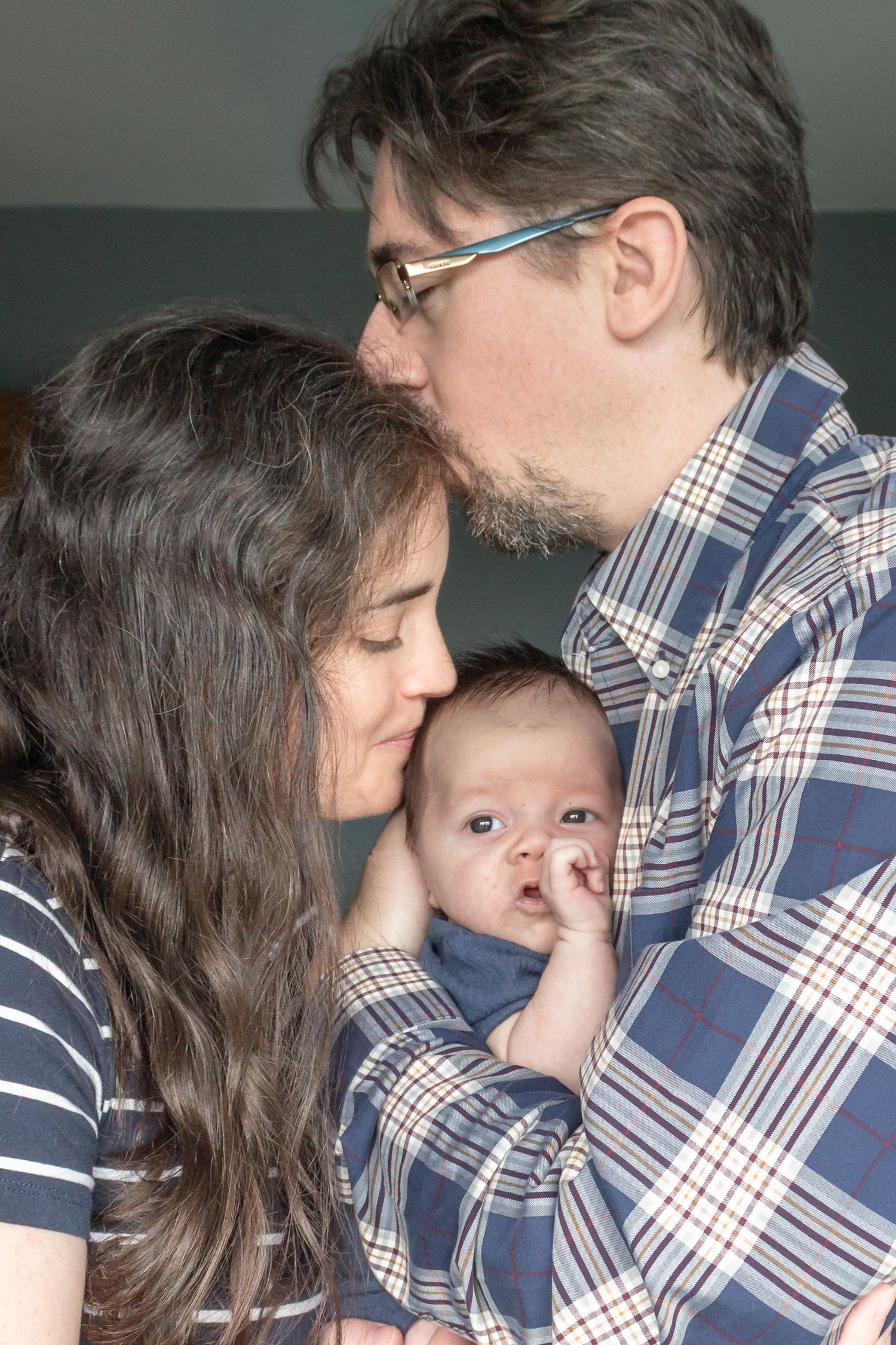 Mother and father cuddling their newborn baby during an intimate lifestyle newborn photography session at home.