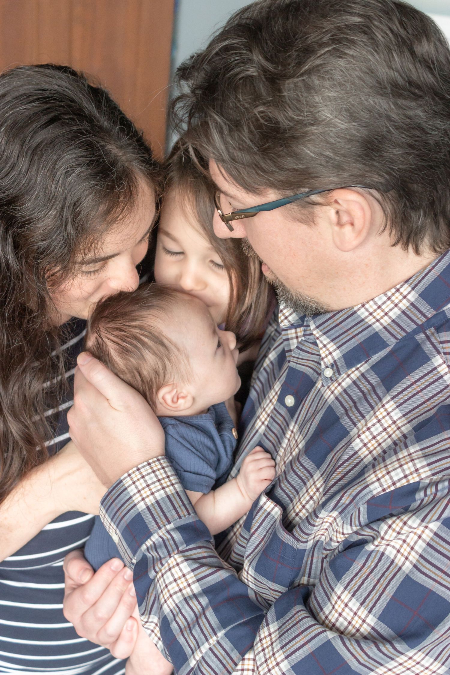 Mother and father gently kissing their newborn baby during a tender in-home lifestyle newborn photography session.