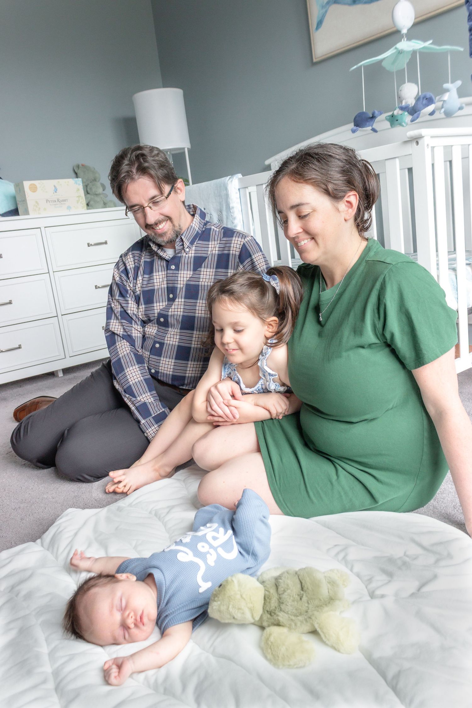 Mother holding her toddler while the father smiles beside them during a candid in-home newborn family photography session.