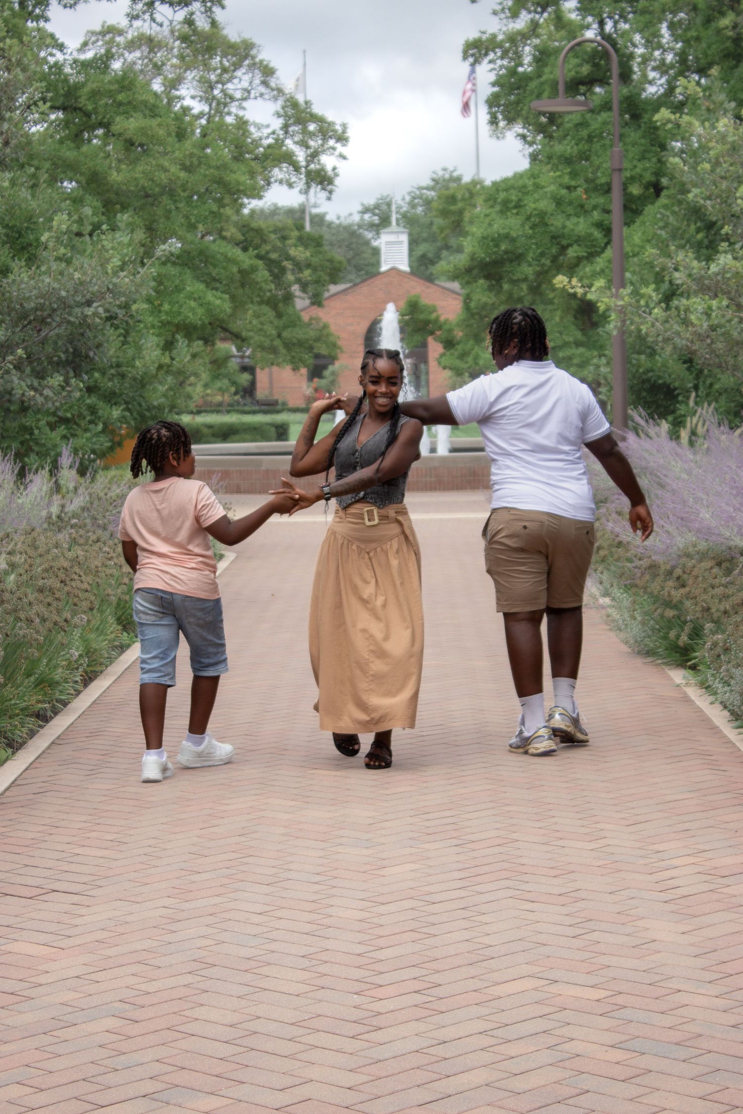 Mother walking hand in hand with her two children along a brick park pathway during a playful outdoor family photography session.