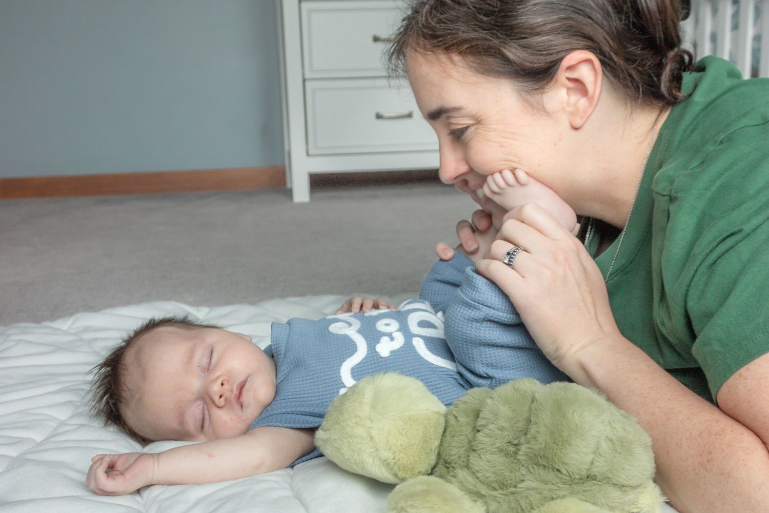 Mother gently kissing her sleeping baby on a bed during a tender in-home newborn photography session.