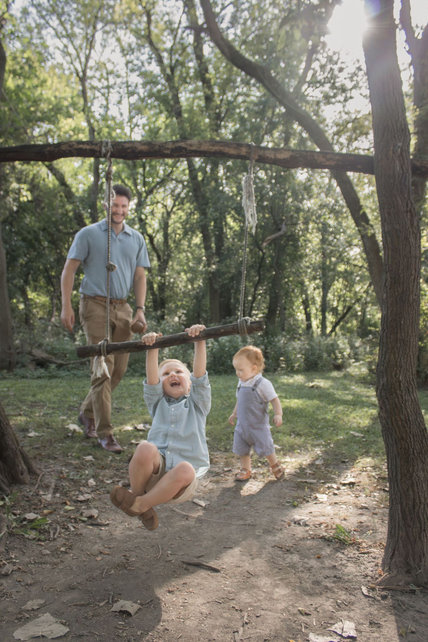 Family of four exploring a wooded trail, with two young children playing beneath the trees during a candid outdoor family photo session.