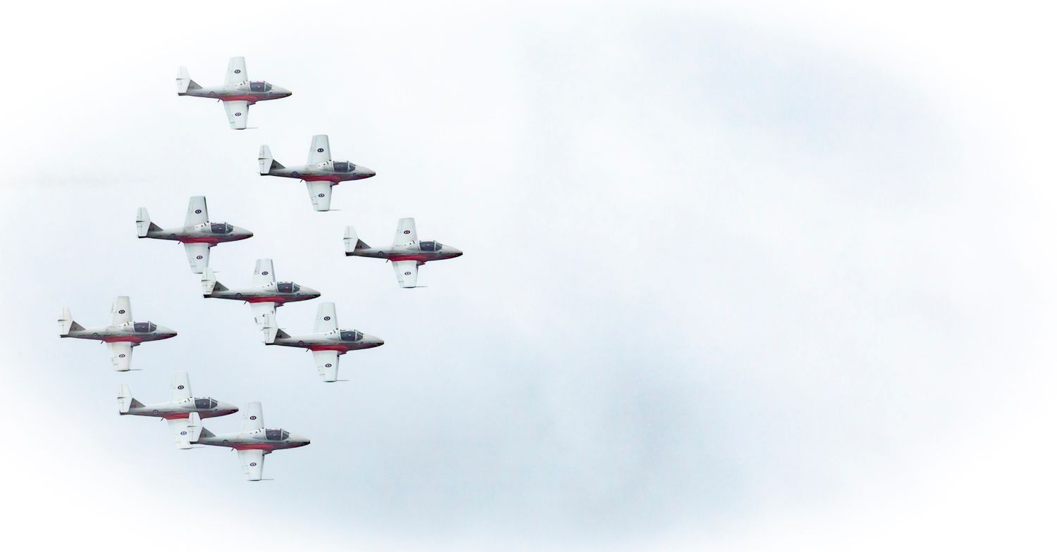 Nine red and white aerobatic planes flying in tight diamond formation against a pale overcast sky.