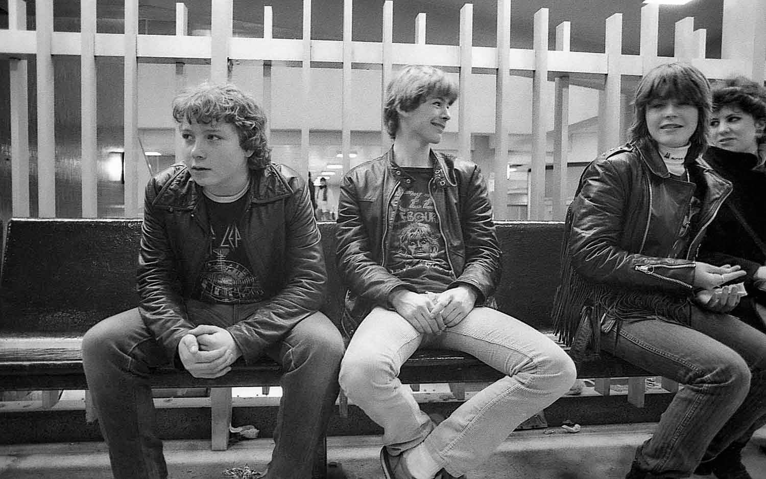 Black and white vintage photo of young people in leather jackets sitting on bleachers at a public event.