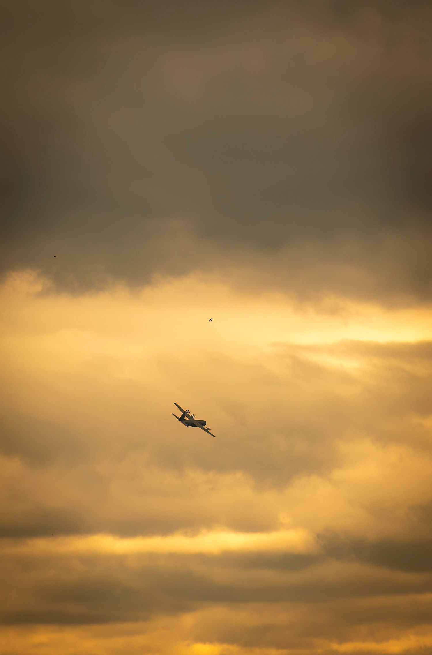 A military aircraft flying through golden sunset clouds in dramatic light.