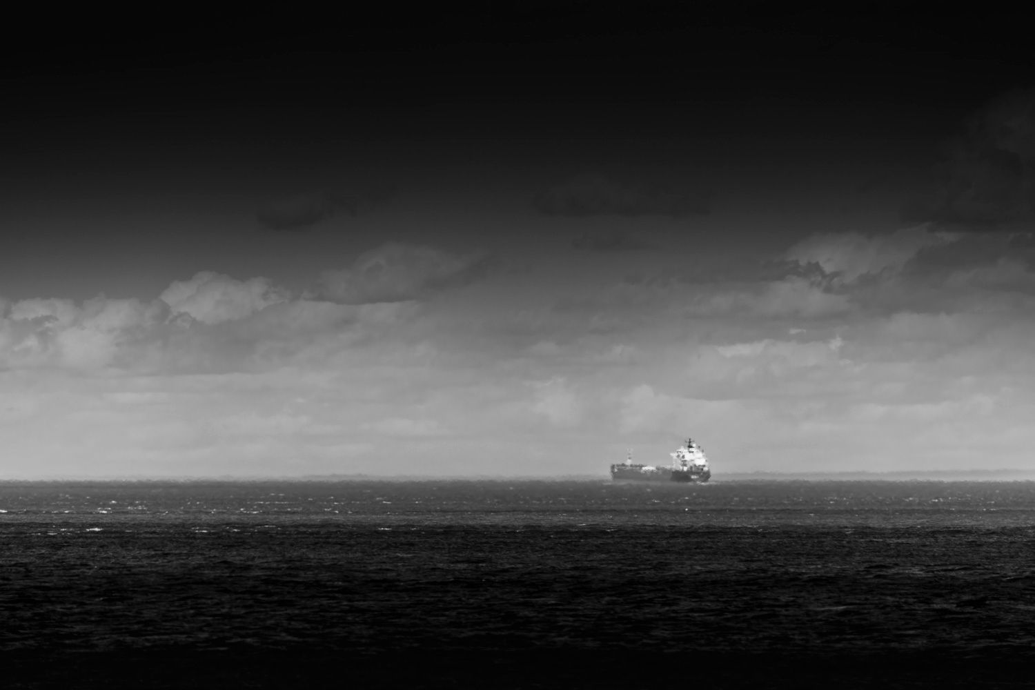 Vaisseau fantôme
Black and white photo of a cargo ship sailing on a vast ocean under a dramatic cloudy sky.
