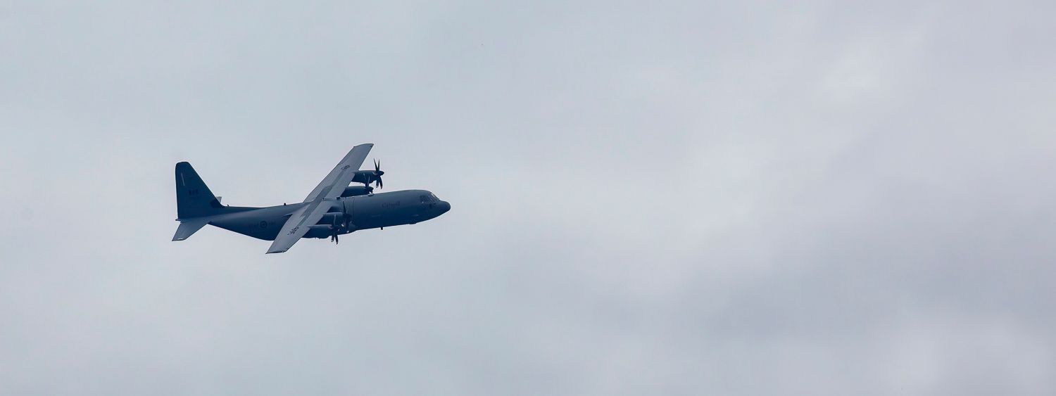 A C-130 Hercules military transport aircraft flying against overcast skies.