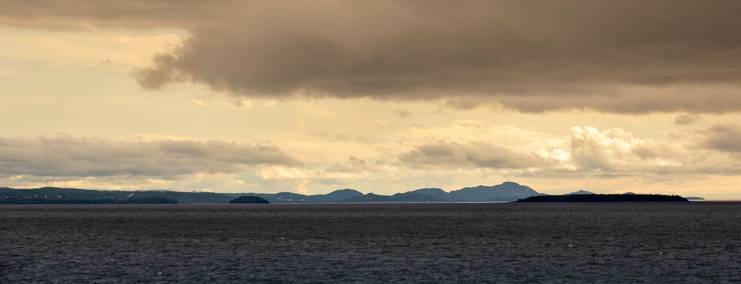 Panoramic view of distant mountains silhouetted against a dramatic golden cloudy sky over the sea.